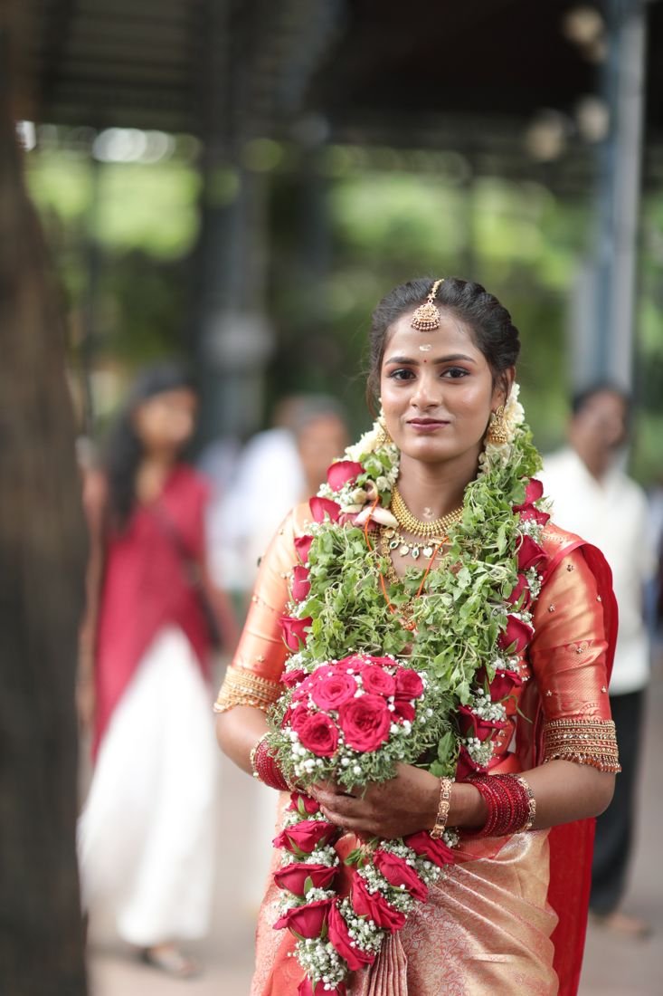 Guruvayur bridal makeup - bride in orange silk saree holding rose bouquet