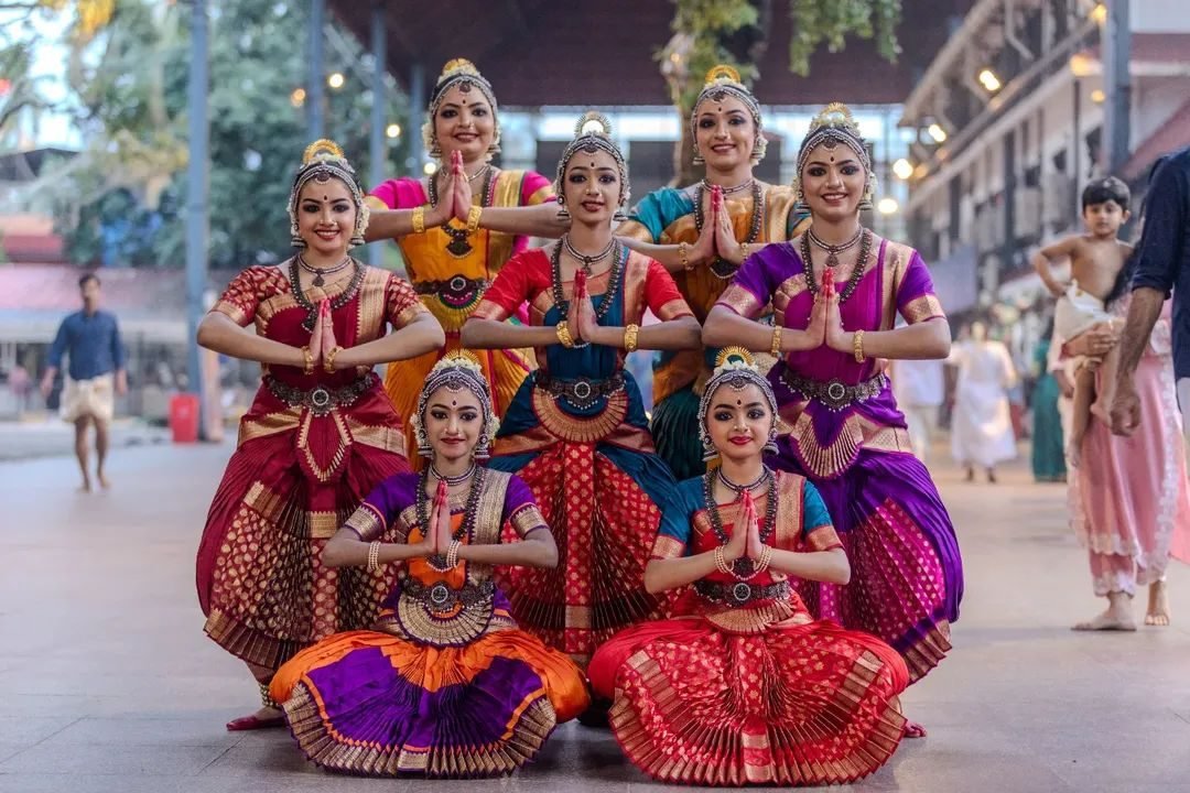 Group dance makeup Guruvayur - seven Bharatanatyam dancers in namaskaram pose in colourful silk
