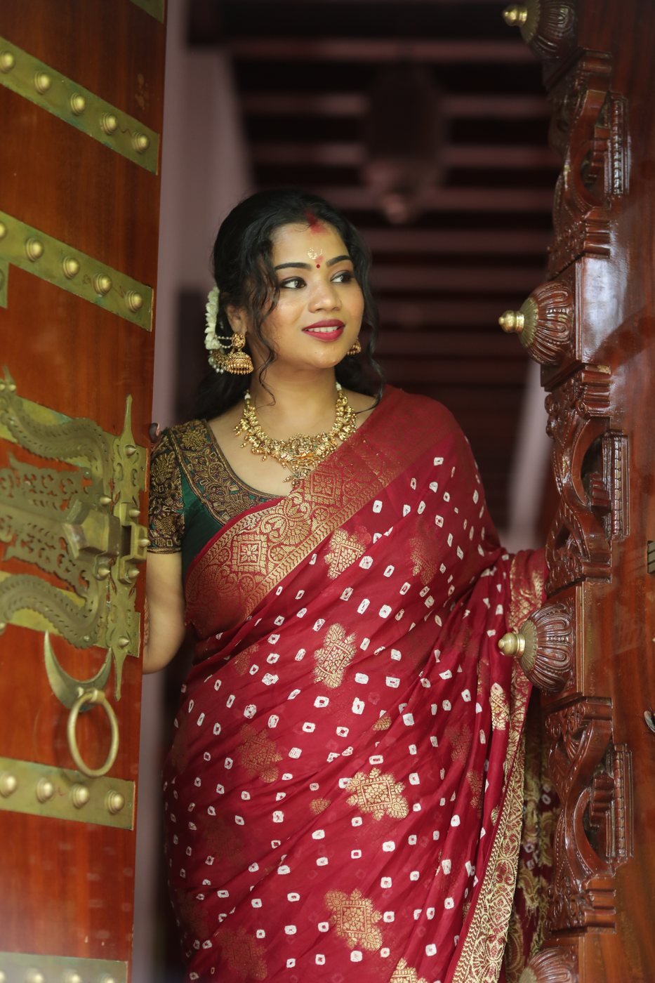Guest look makeup Guruvayur - woman in red bandhani saree at a carved wooden door